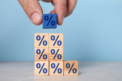 Image of Man putting blue cube with percent sign onto others against light blue background, closeup