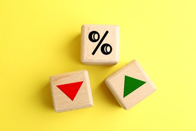 Image of Wooden cubes with percent sign, up and down arrows on yellow background, top view