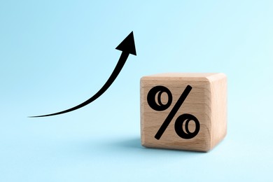Image of Percent sign on wooden cube and arrow against light blue background