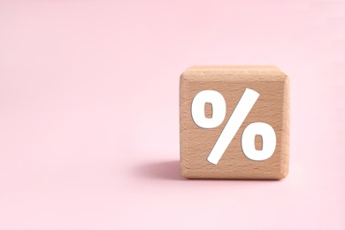 Image of Percent sign on wooden cube against pink background. Space for text