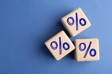 Image of Wooden cubes with percent signs on blue background, top view. Space for text