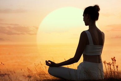 Image of Woman meditating in lotus position outdoors against sunset sun