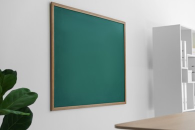 Photo of Blank green chalkboard, desk and shelving unit in classroom