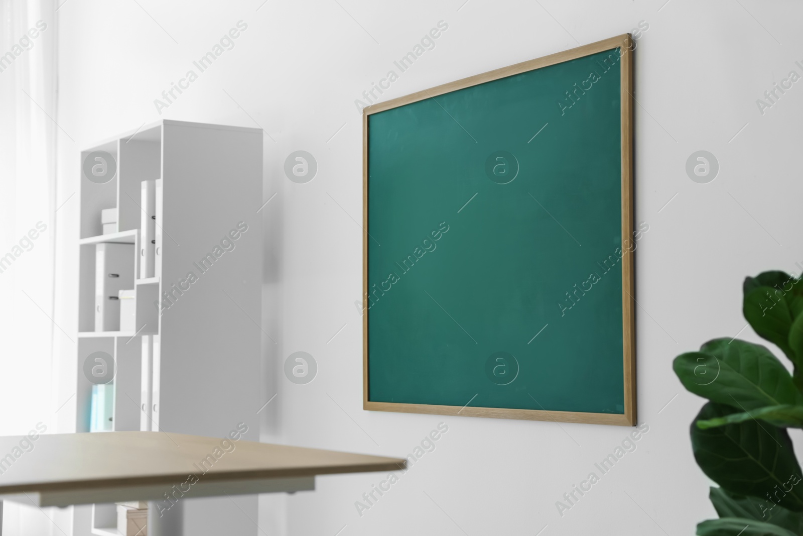 Blank green chalkboard, desk and shelving unit in classroom Photo of Blank green chalkboard, desk and shelving unit in classroom