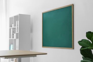 Photo of Blank green chalkboard, desk and shelving unit in classroom
