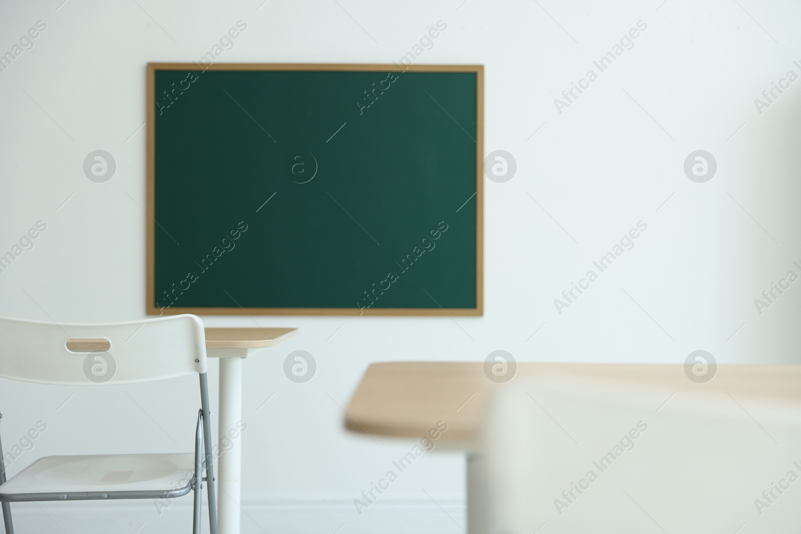 Blank green chalkboard, desks and chairs in classroom Photo of Blank green chalkboard, desks and chairs in classroom