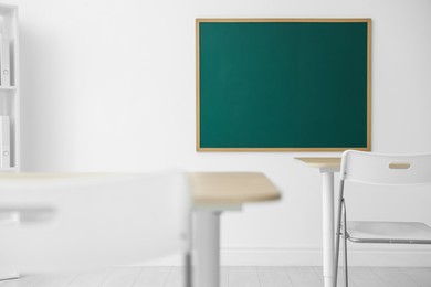 Photo of Blank green chalkboard, desks and chairs in classroom