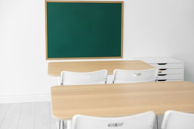 Photo of Blank green chalkboard, desks and chairs in classroom