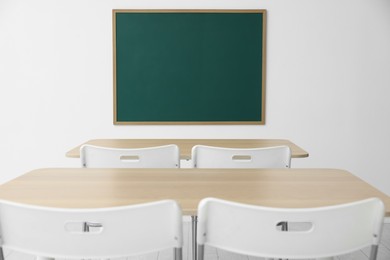 Photo of Blank green chalkboard, desks and chairs in classroom