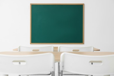 Photo of Blank green chalkboard, desks and chairs in classroom