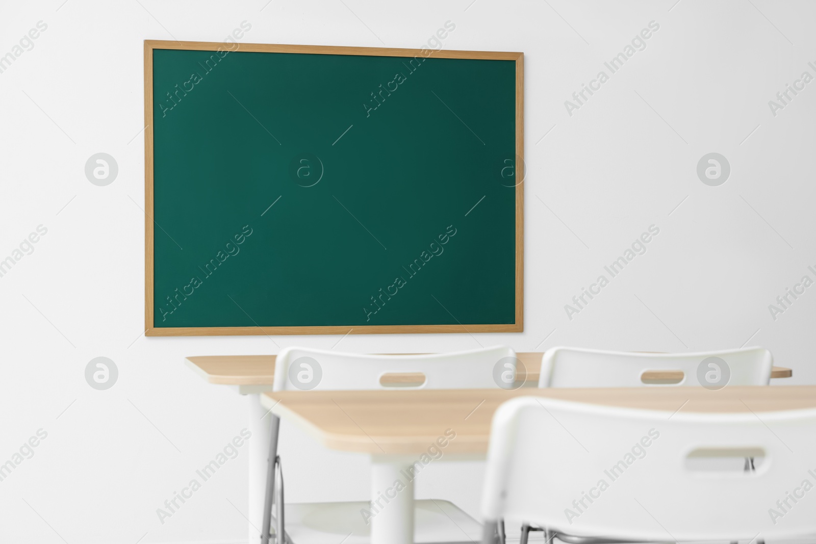 Blank green chalkboard, desks and chairs in classroom Photo of Blank green chalkboard, desks and chairs in classroom