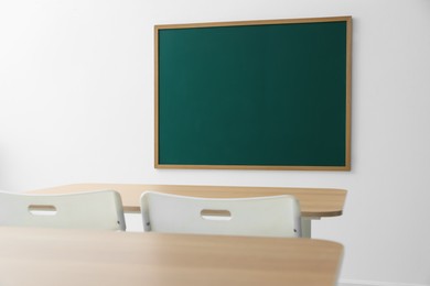 Photo of Blank green chalkboard, desks and chairs in classroom