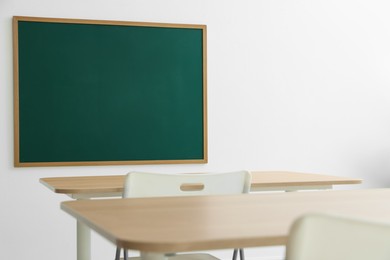 Photo of Blank green chalkboard, desks and chairs in classroom