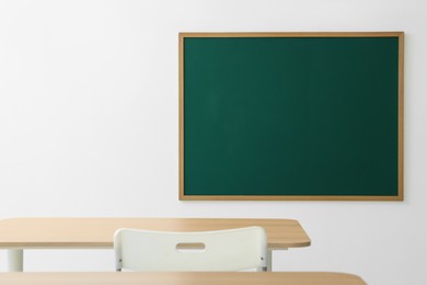 Photo of Blank green chalkboard, desks and chair in classroom
