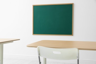 Photo of Blank green chalkboard, desks and chair in classroom