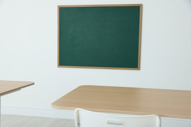 Photo of Blank green chalkboard, desks and chair in classroom