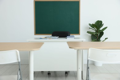 Photo of Blank green chalkboard, desks, chairs and plant in classroom