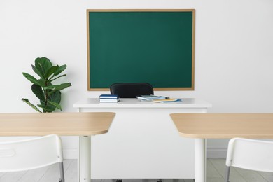 Photo of Blank green chalkboard, desks, chairs and plant in classroom