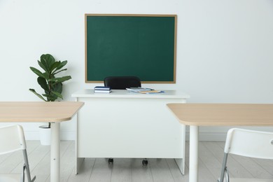 Photo of Blank green chalkboard, desks, chairs and plant in classroom