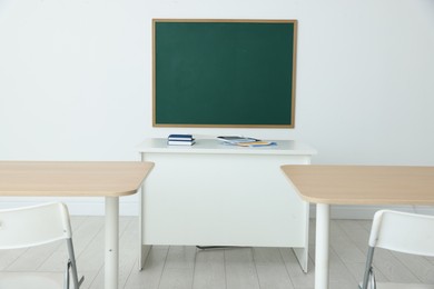 Photo of Blank green chalkboard, desks and chairs in classroom