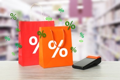 Image of Shopping bags with percent signs and payment terminal on counter in store