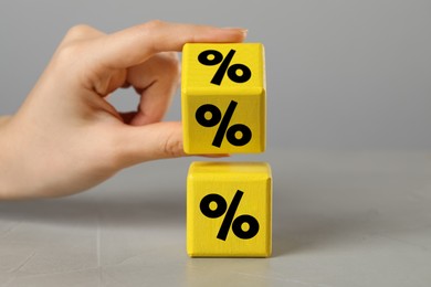 Image of Woman holding yellow cube with percent signs on grey background, closeup
