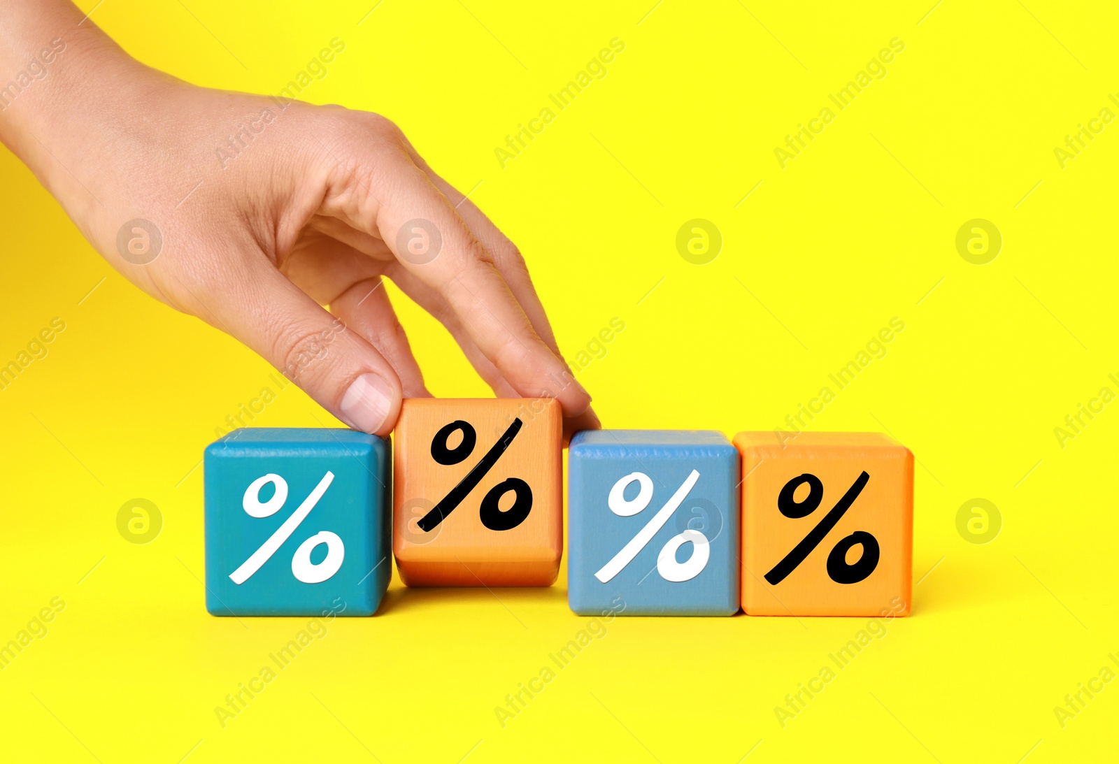 Image of Woman holding orange cube with percent sign among others on yellow background, closeup