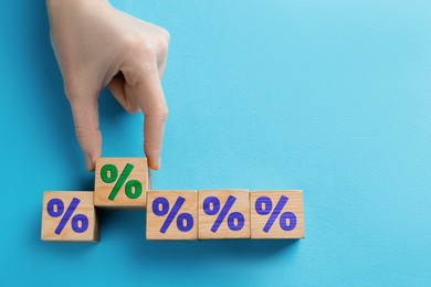 Image of Woman holding wooden cube with green percent sign among others on light blue background, top view