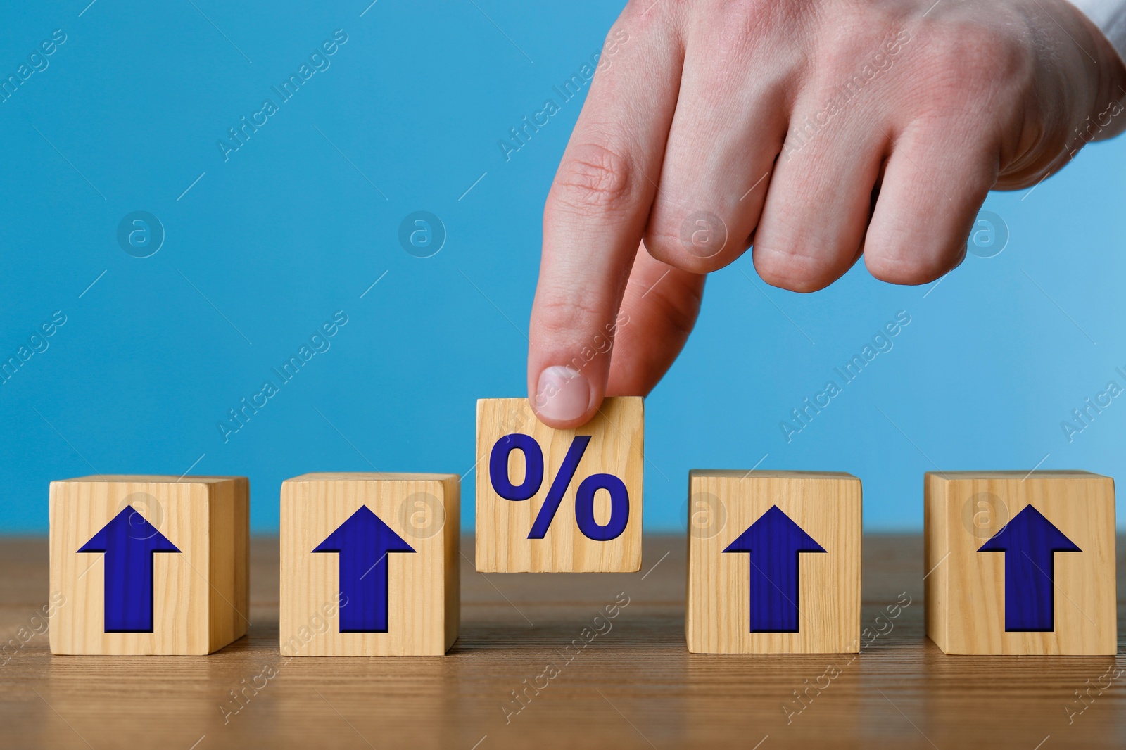 Image of Man putting wooden cube with percent sign among others with arrows against blue background, closeup