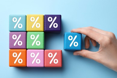 Image of Woman putting cube with percent sign to others on light blue background, top view