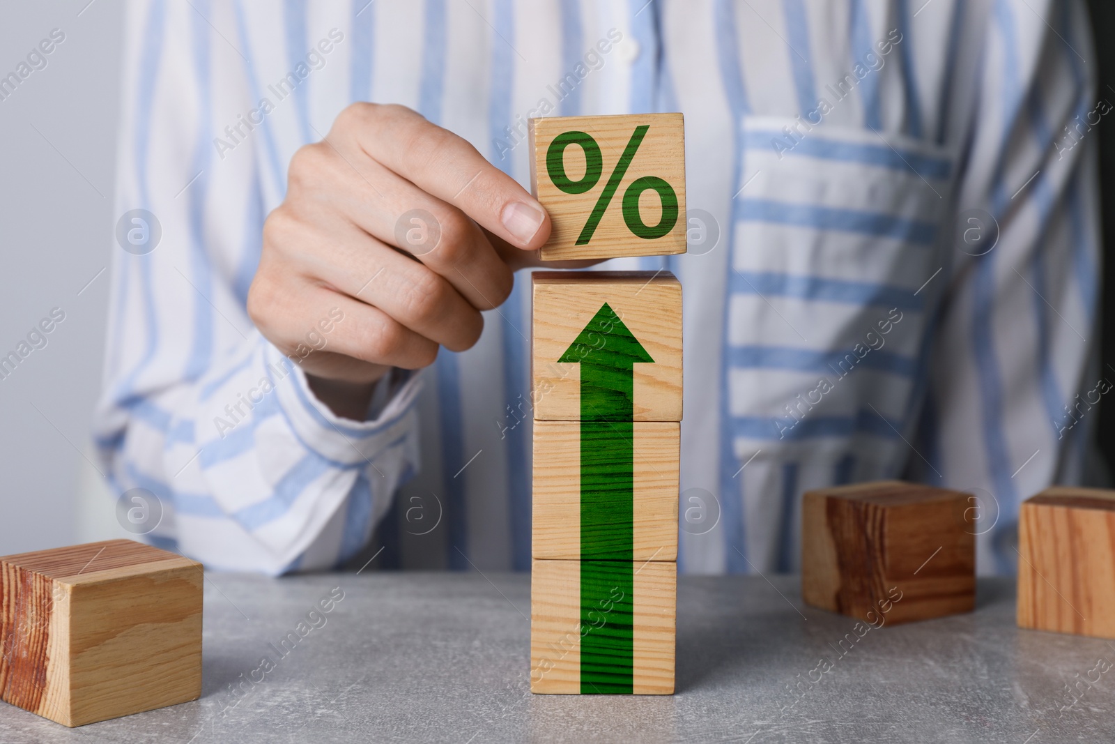 Image of Woman putting wooden cube with percent sign on top of others at table, closeup