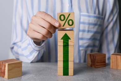 Image of Woman putting wooden cube with percent sign on top of others at table, closeup