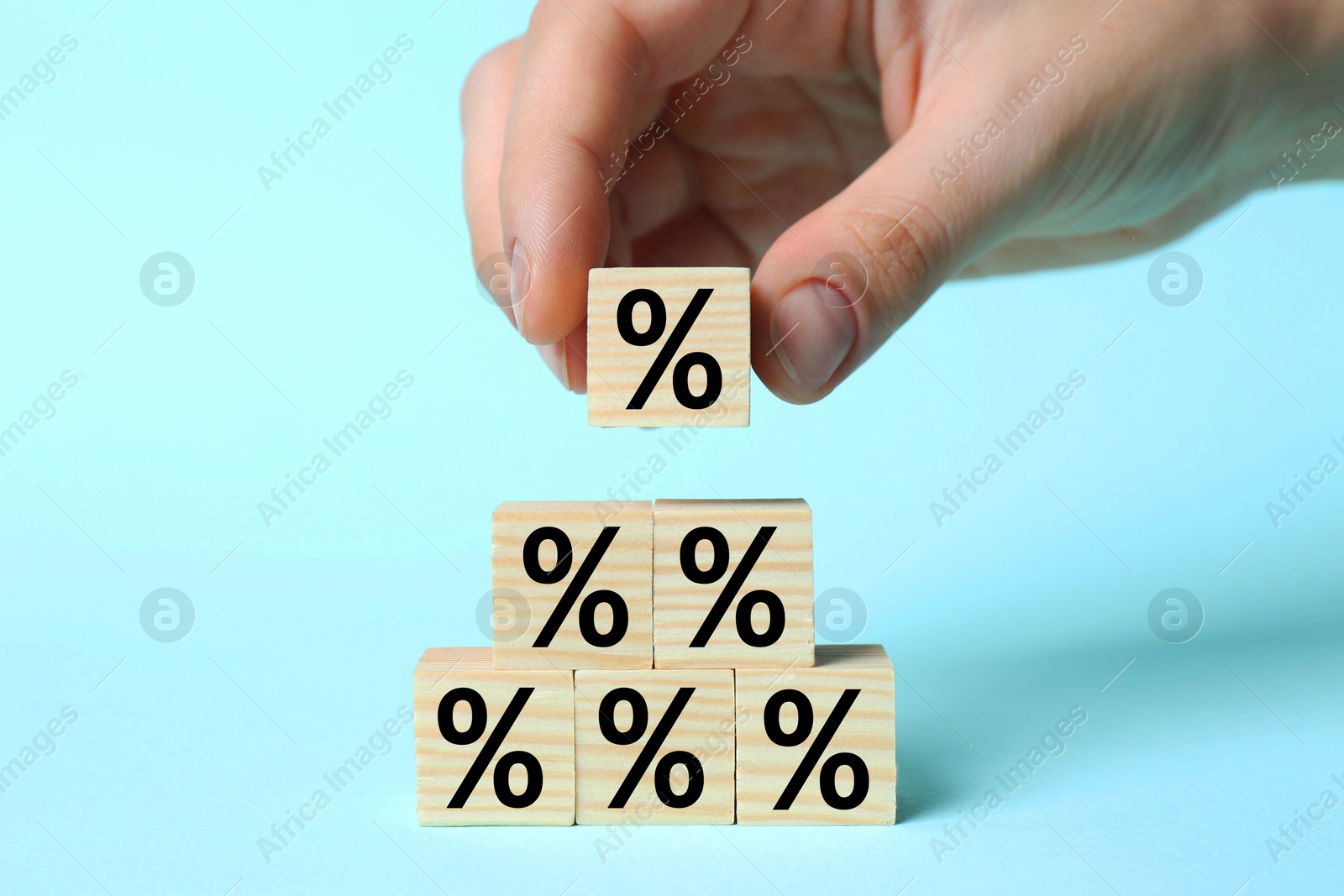 Man putting wooden cube with percent sign onto others against light blue background, closeup Image of Man putting wooden cube with percent sign onto others against light blue background, closeup