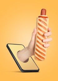 Image of Food ordering and delivery service. Woman's hand with tasty French hot dog, sticking out of mobile phone display against orange background, closeup