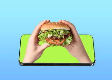 Image of Food ordering and delivery service. Woman's hands with burger, sticking out of mobile phone display against blue gradient background, closeup