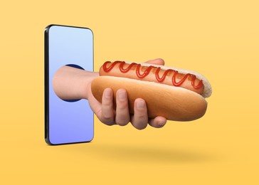 Image of Food ordering and delivery service. Woman's hand with tasty hot dog, sticking out of mobile phone display against orange background, closeup