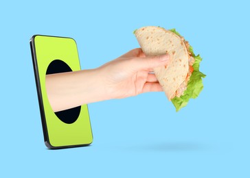 Image of Food ordering and delivery service. Woman's hand with tasty taco, sticking out of mobile phone display against light blue background, closeup
