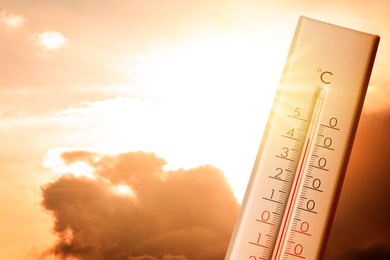 Image of High temperature on thermometer against orange sky on sunny day. Hot summer weather