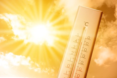 Image of High temperature on thermometer against orange sky on sunny day. Hot summer weather