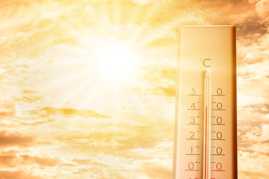 Image of High temperature on thermometer against orange sky on sunny day. Hot summer weather