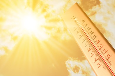 Image of Extremely high temperature on thermometer against orange sky on sunny day. Severely hot summer weather