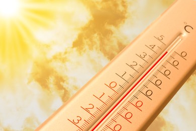 Image of Extremely high temperature on thermometer against orange sky on sunny day. Severely hot summer weather