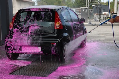 Photo of Man washing auto with high pressure water jet at car wash, closeup