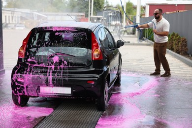Photo of Man washing auto with high pressure water jet at car wash