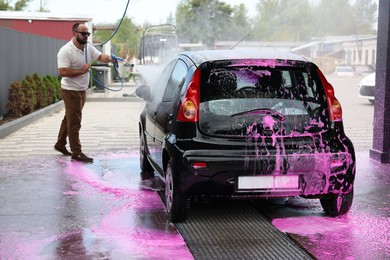Photo of Man washing auto with high pressure water jet at car wash