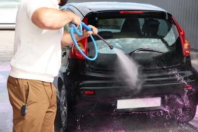 Photo of Man washing auto with high pressure water jet at car wash, closeup
