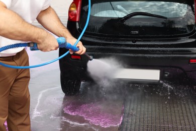Photo of Man washing auto with high pressure water jet at car wash, closeup