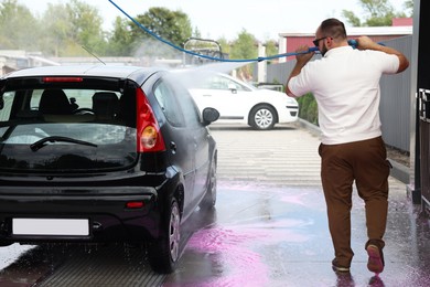 Photo of Man washing auto with high pressure water jet at car wash