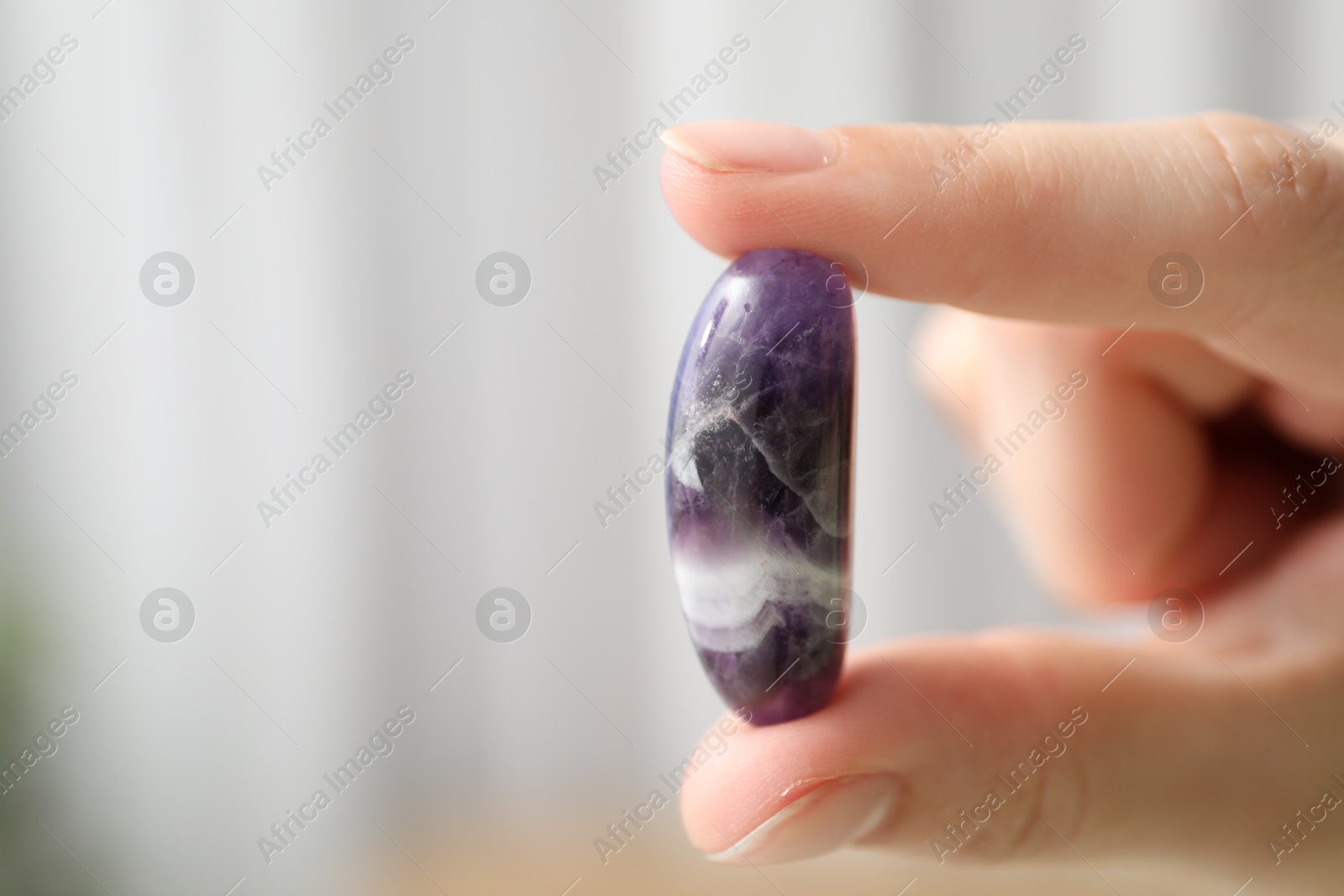 Photo of Woman with healing stone on blurred background, closeup. Space for text