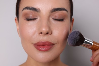 Photo of Beautiful woman with makeup brush on light grey background, closeup